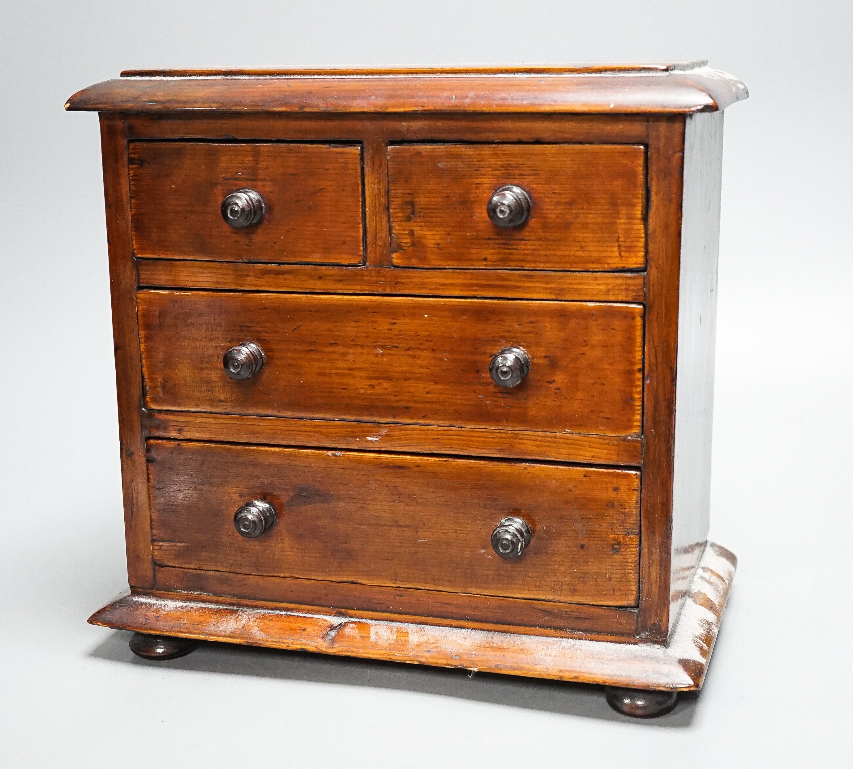 A Victorian stained pine miniature chest of drawers, 27 cms high.